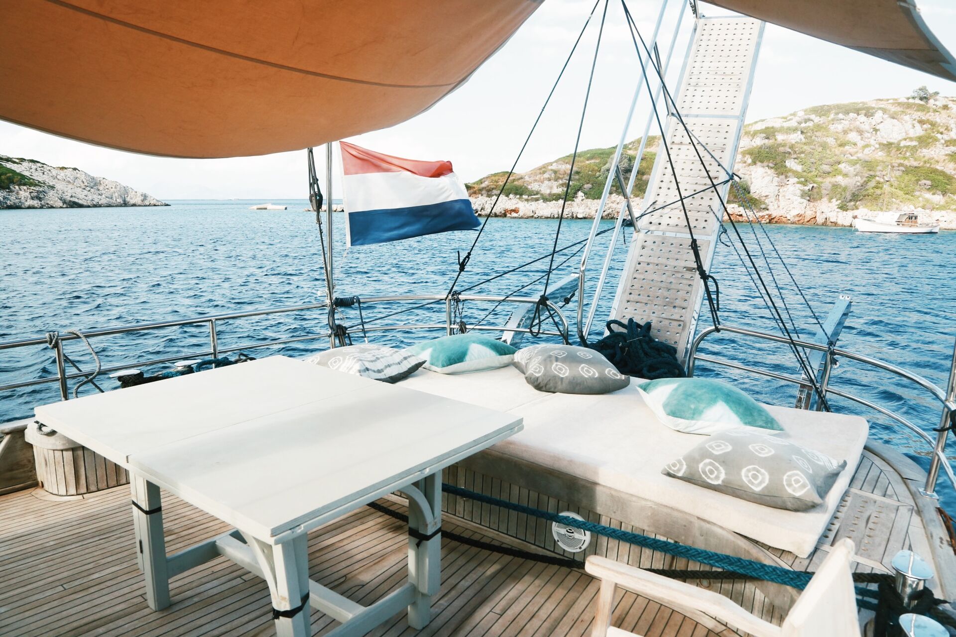 The aft deck of Sea Moon with sunbed, canopy and dining table in a rocky cove