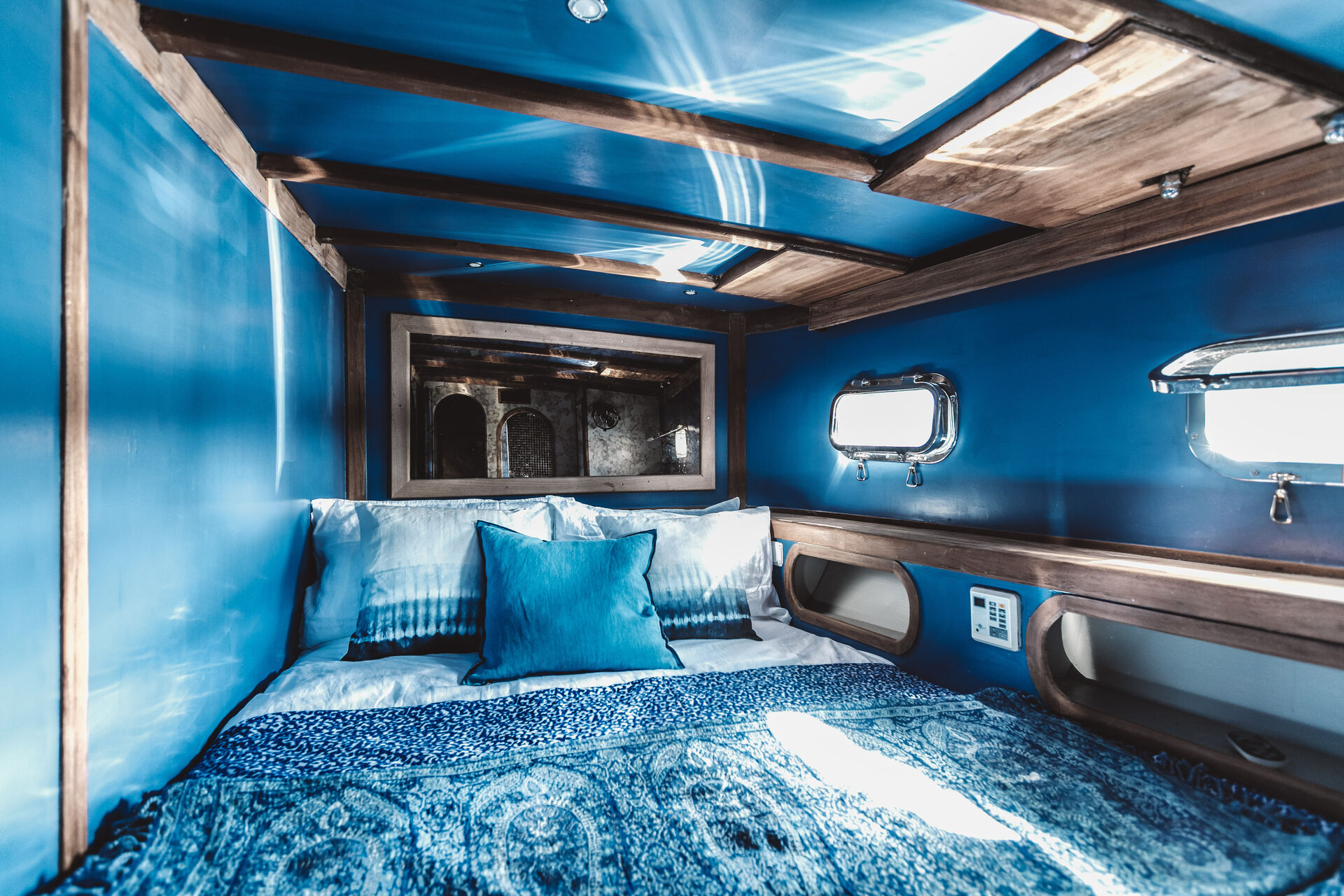 A blue-painted cabin with wooden beams, a mirror and portholes