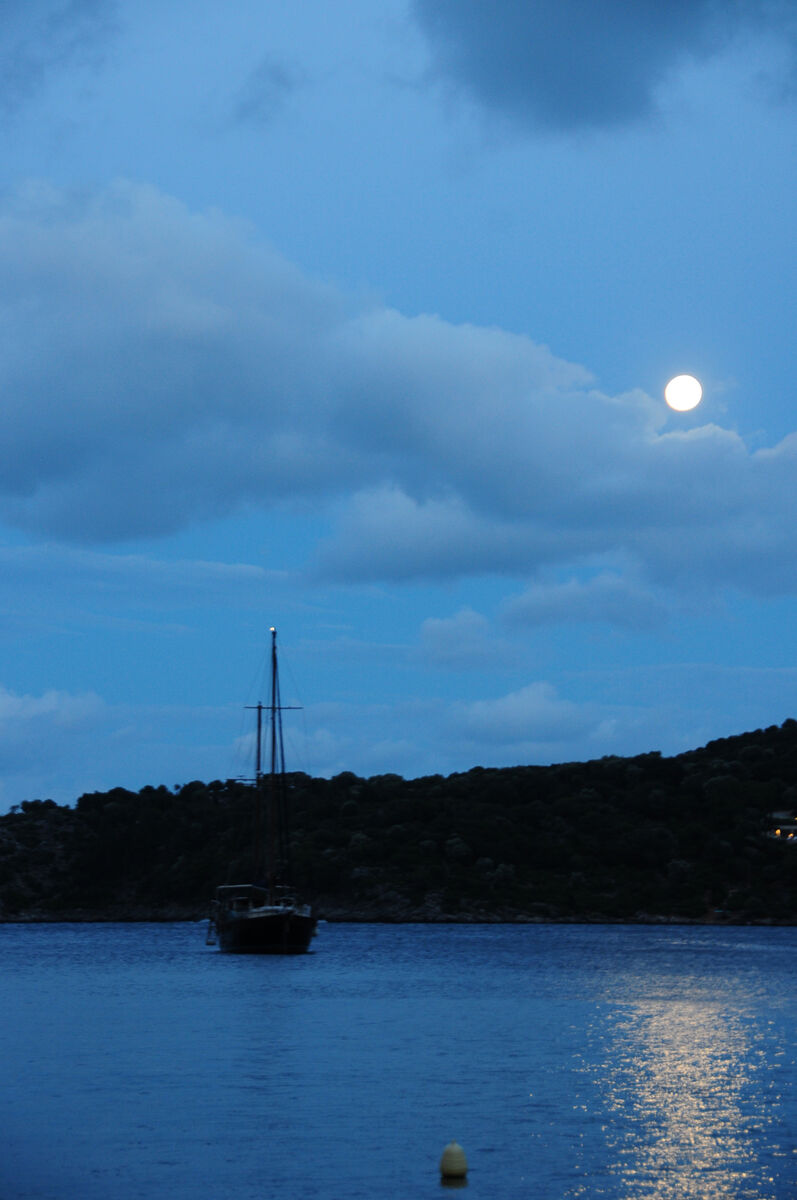 A sailboat anchored in a cove under a full moon at night
